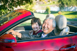 Smiling older couple in a red convertible, representing safe and confident driving in later years with proper vision care