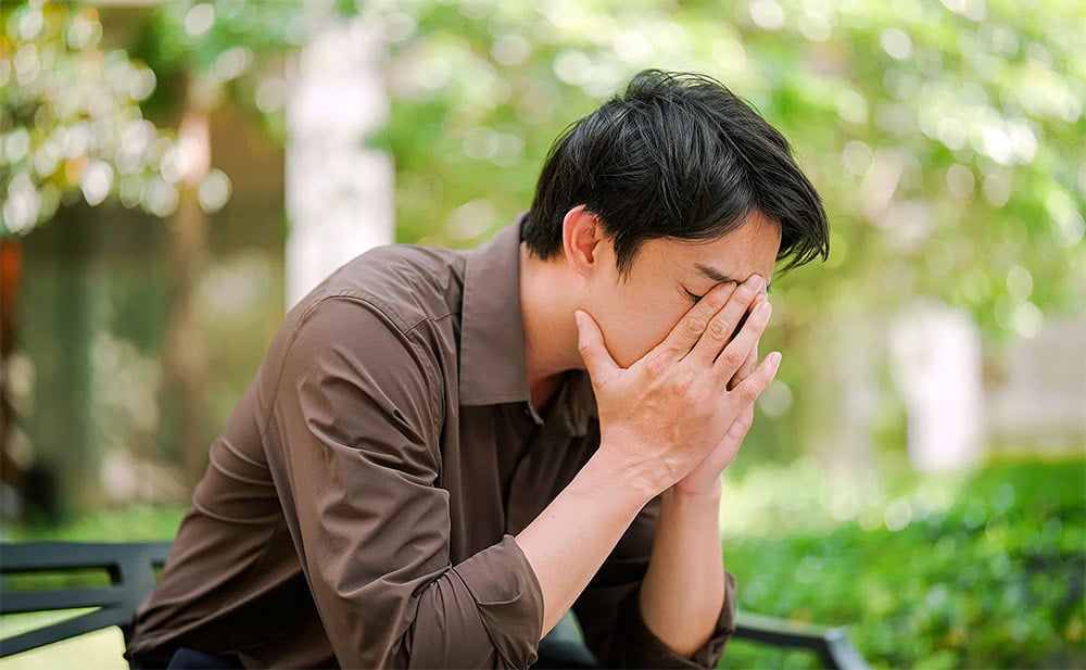 Man rubbing eyes in public park representing eyelid pain causes from dry eye