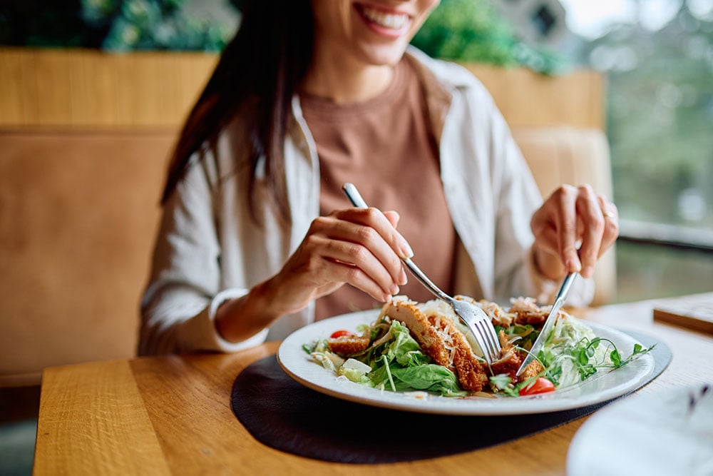 Woman enjoying a healthy chicken salad with leafy greens and vegetables that provide vitamins for eye health.