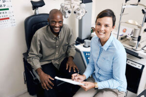 An optometrist smiles while reviewing notes with a patient in an exam room, illustrating patient education on antibiotic eye drop use