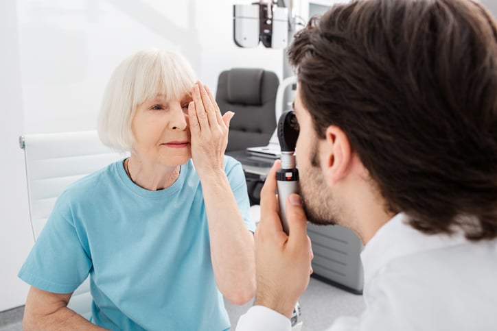 Older woman covering one eye while a male eye doctor performs a cataract exam with a handheld light during a routine vision evaluation. Learn more about cataracts and eye health at Wellish Abrams Vision Institute