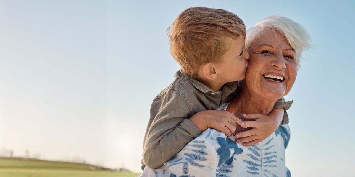 Woman with grandchild on back and excited to see clear vision after cataract surgery thanks to their ophthalmologist.