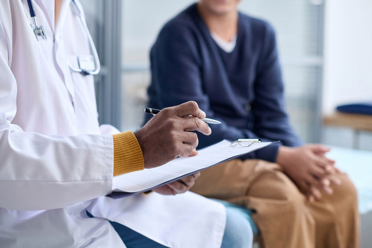 Eye doctor reviews notes on a clipboard while meeting with a patient during a LASIK consultation in a clinical exam room.