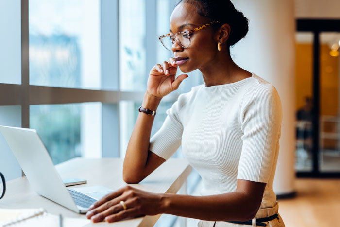 Professional woman wearing glasses reviews LASIK cost information on a laptop in a bright, modern setting.