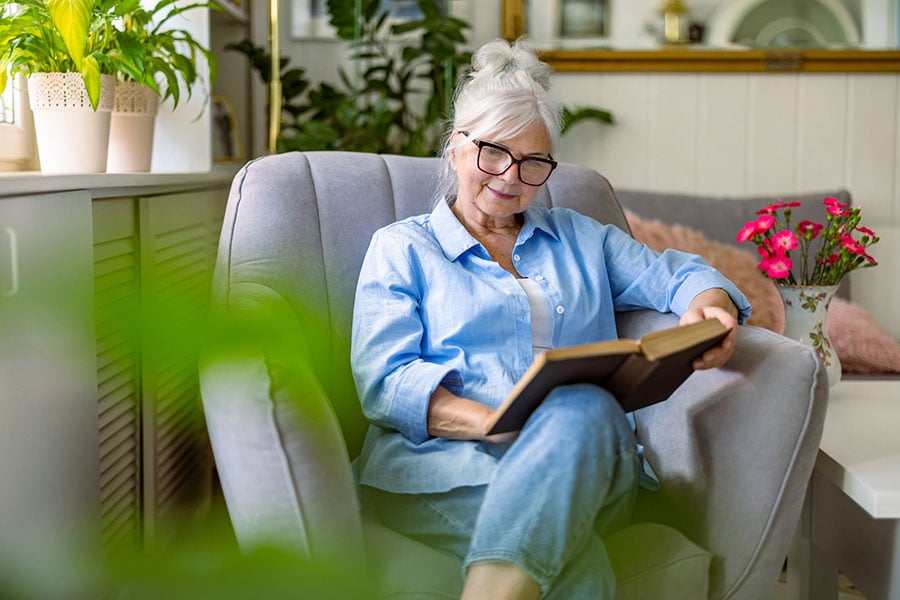 Woman contemplating cataract surgery after having blurry vision on the couch trying to read a book.