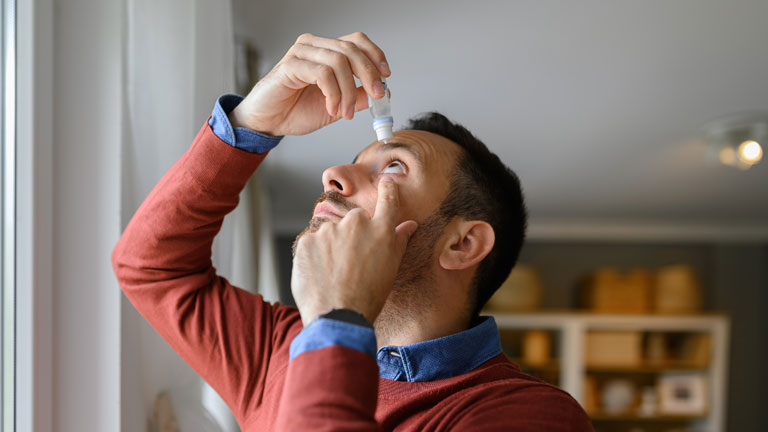 Man administering glaucoma eye drops into his eye as part of a daily treatment routine to help lower intraocular pressure and protect vision.