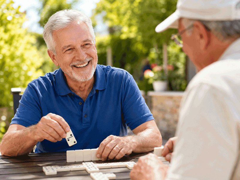 Senior man laughing while playing dominoes with a friend outdoors, illustrating quality-of-life goals after glaucoma specialist care in Las Vegas at Wellish Abrams Vision Institute.